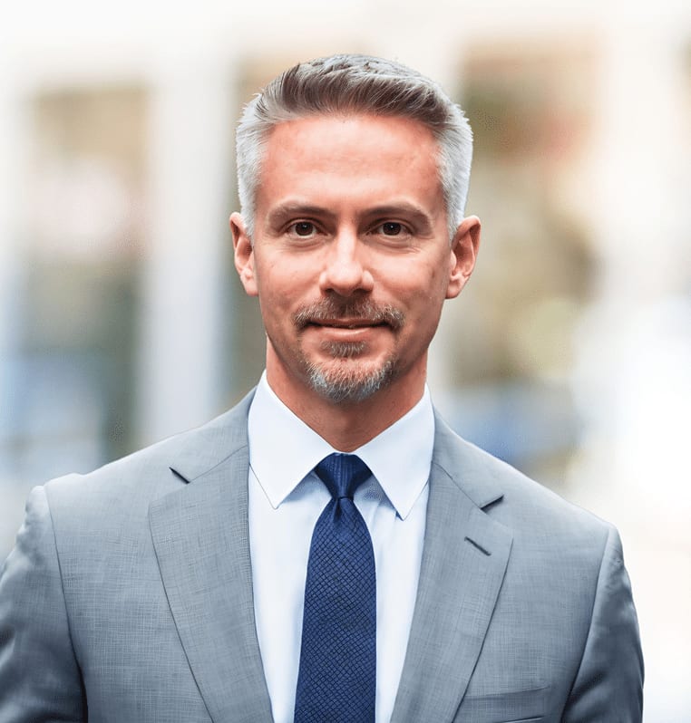 Professional man in a grey suit and blue tie, with grey hair and goatee, looking at the camera.