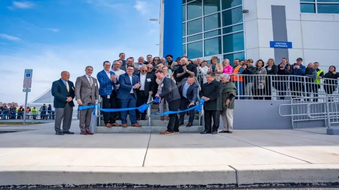 Group of people cutting a blue ribbon at a grand opening event for a modern building.