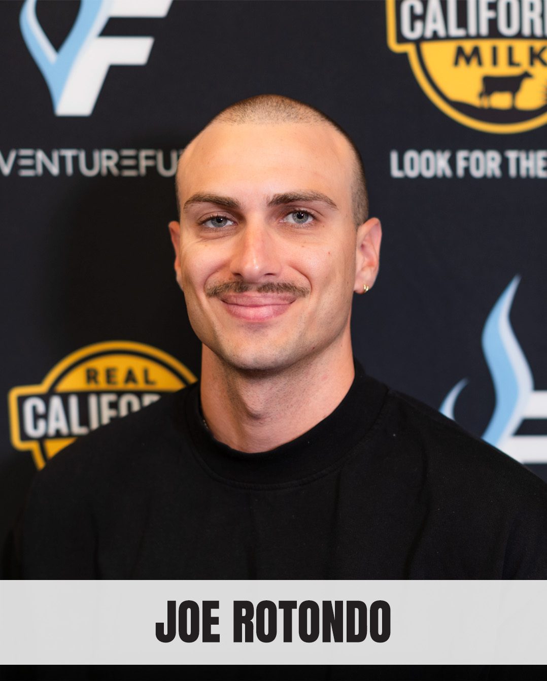 Portrait of Joe Rotondo, a man with a shaved head and mustache, smiling at the camera.