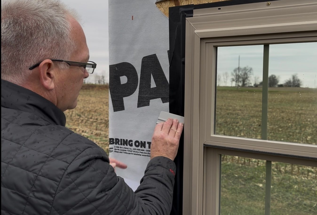 Man applying seal around a window frame next to house wrap.