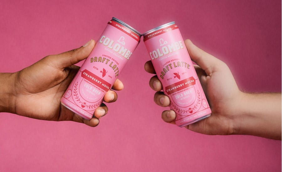 Two hands clinking pink La Colombe Strawberry Mocha Draft Latte cans.