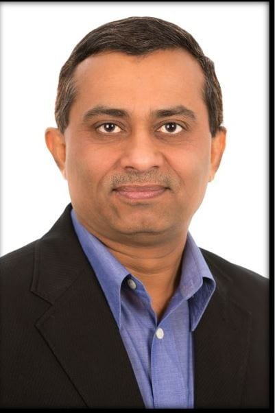 A headshot of a smiling man in a blue shirt and dark blazer against a white background.