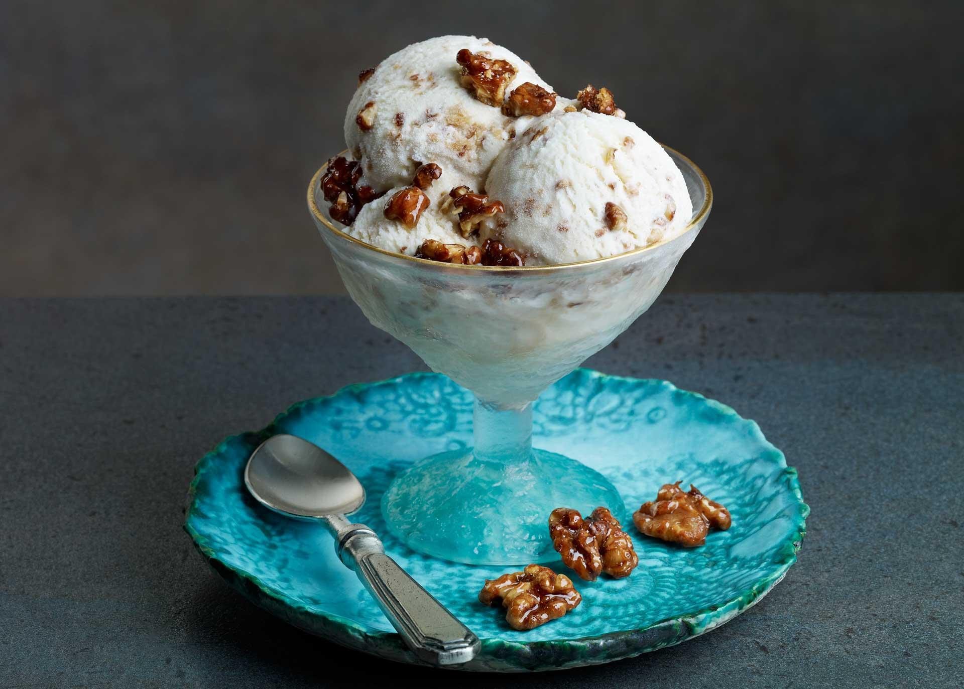 Ice cream with candied walnuts in a frosted glass bowl on a teal plate, with a spoon.