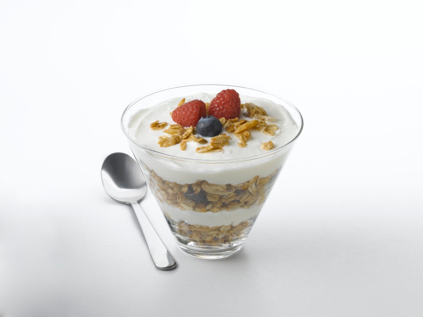Yogurt parfait layered with granola, raspberries, and a blueberry, with a spoon.