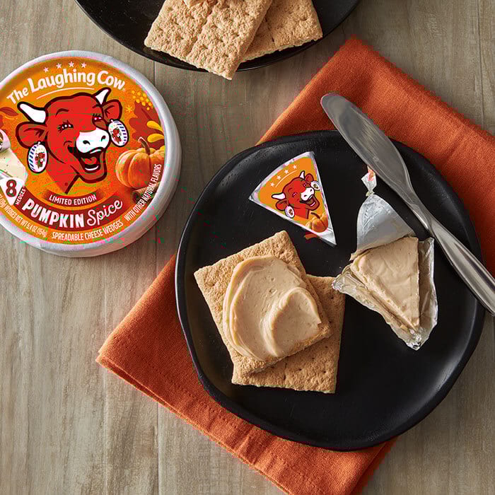 The Laughing Cow Pumpkin Spice cheese, spread on crackers, with an unwrapped wedge on a plate.