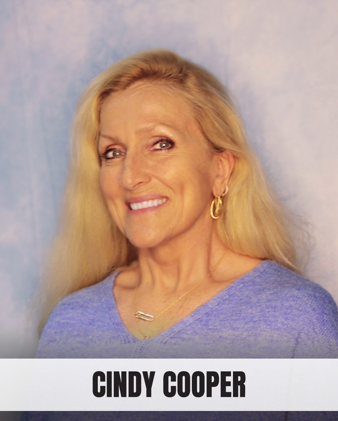 Smiling woman with long blonde hair, wearing a blue sweater and gold earrings.