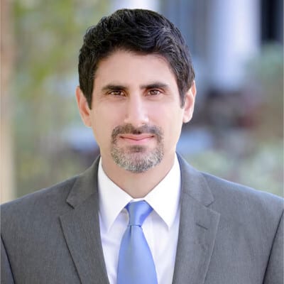Smiling man in a suit and blue tie with dark hair and goatee.
