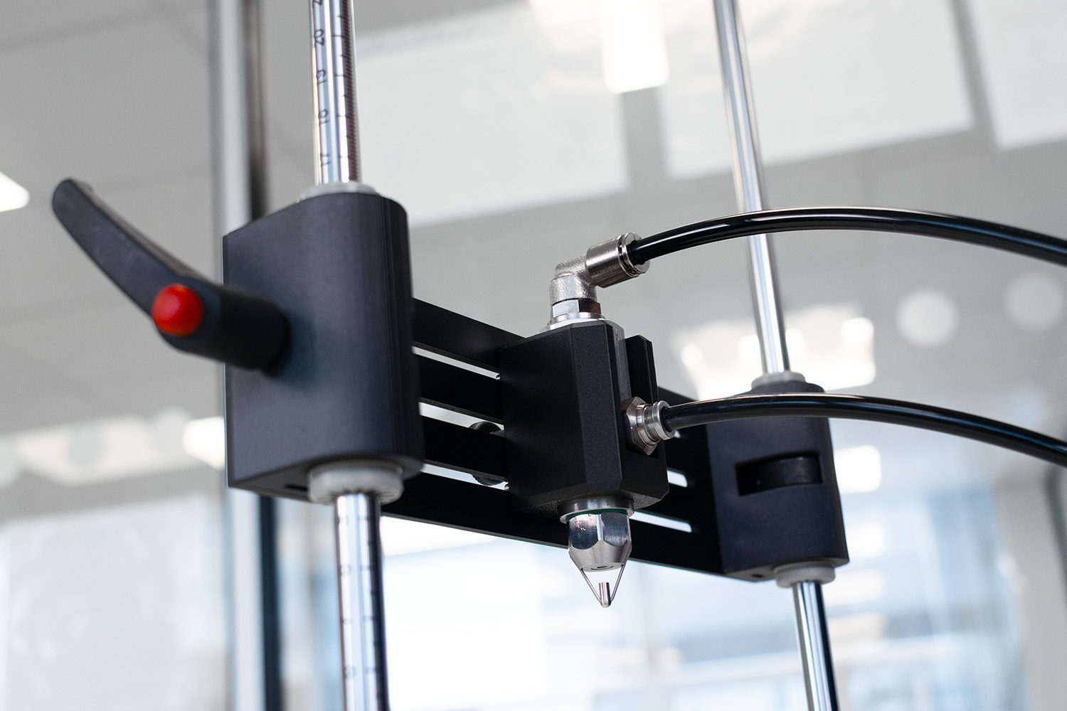 Close-up of a precision machine head with connecting hoses and metal rods, likely for 3D printing or dispensing.
