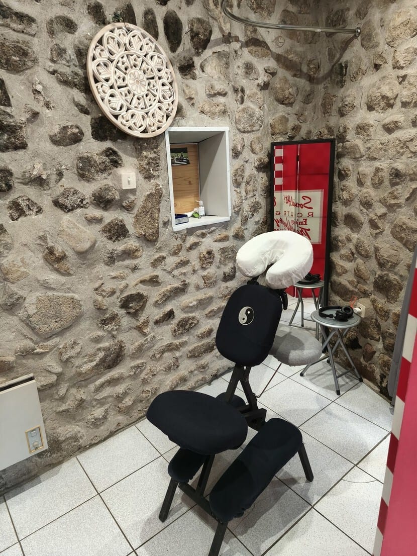 Black massage chair with Yin-Yang symbol in a stone-walled room with mandala decor.