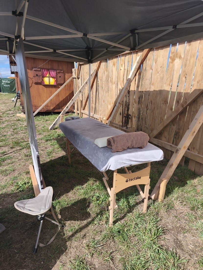 Outdoor massage table under a tent, next to a wooden shed and fence on grass.