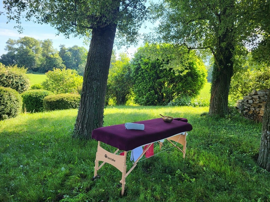 Purple massage table outdoors on green grass under trees.