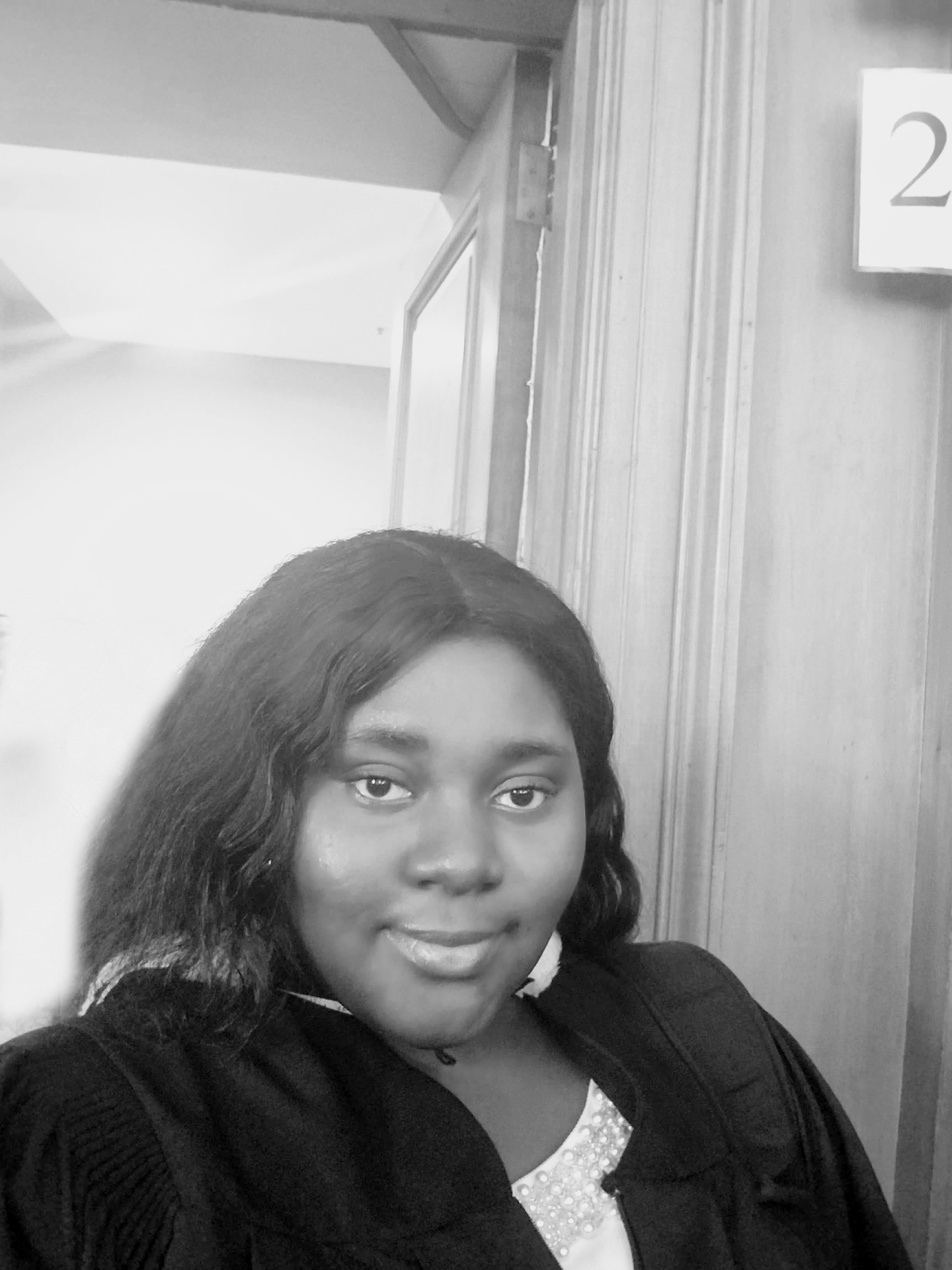 Smiling Black woman in a robe, B&W. Indoors with number '2' on wall.