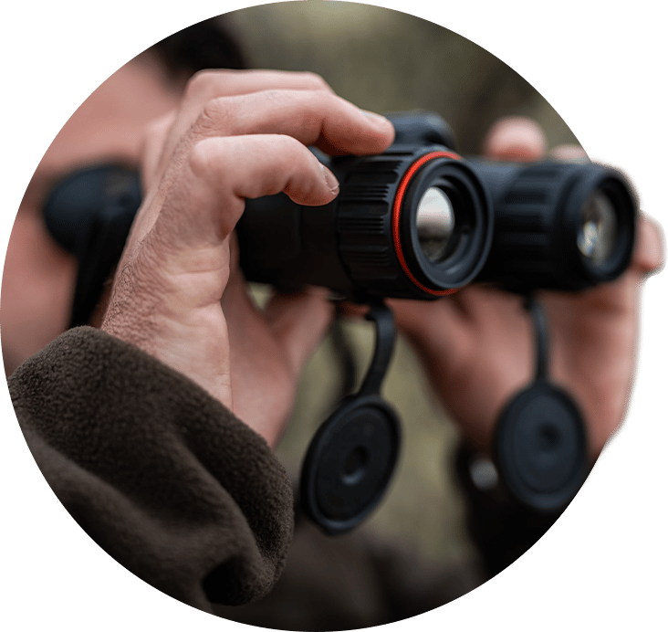 Person holding black binoculars with red accents, hands adjusting them for observation.