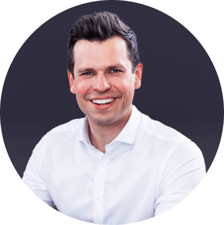Headshot of a man with a wide smile, wearing a white shirt against a dark background.
