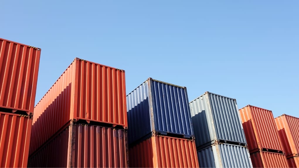 Stacked red, blue, and gray shipping containers under a clear blue sky.