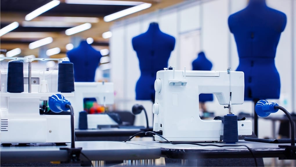 White sewing machines and blue dress forms in a brightly lit sewing workshop.