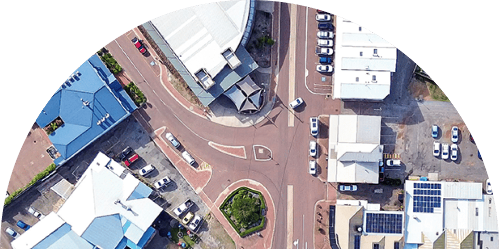 Aerial drone view of a town intersection with commercial buildings, parking lots, and a small roundabout.