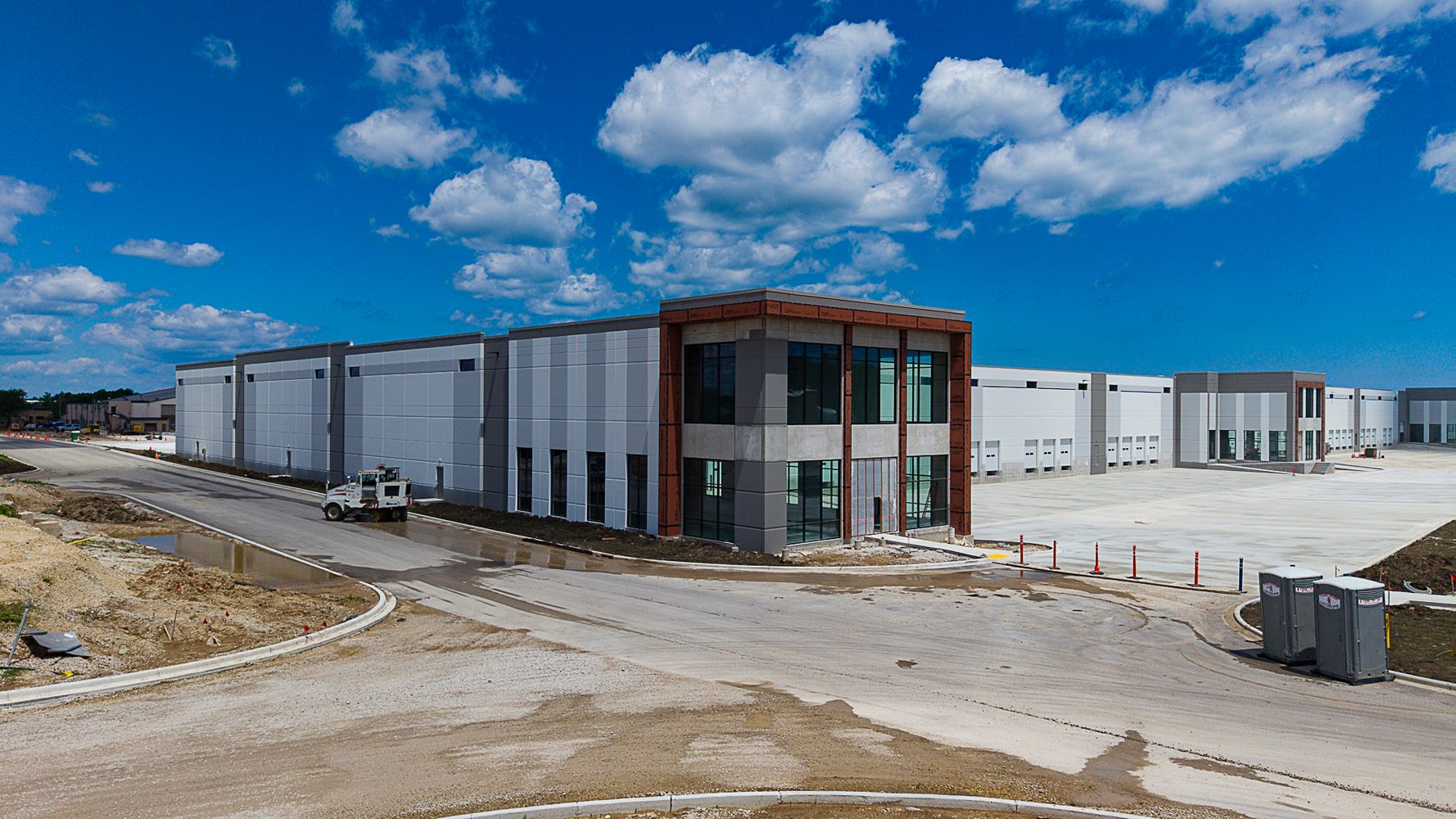 Aerial view of modern industrial warehouses with a new office front and roads under construction.