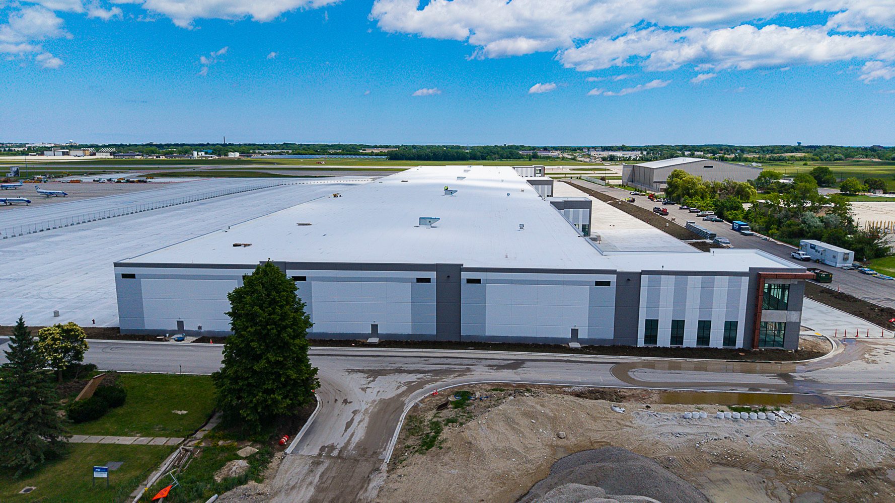 Aerial view of a large modern industrial building next to an airport tarmac with airplanes under a cloudy sky.