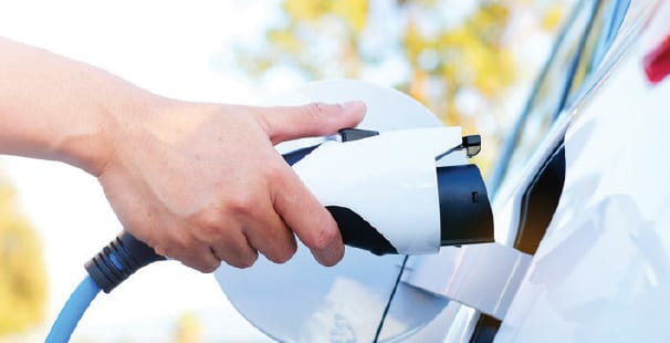 A person's hand plugging an electric vehicle charging cable into a white car.