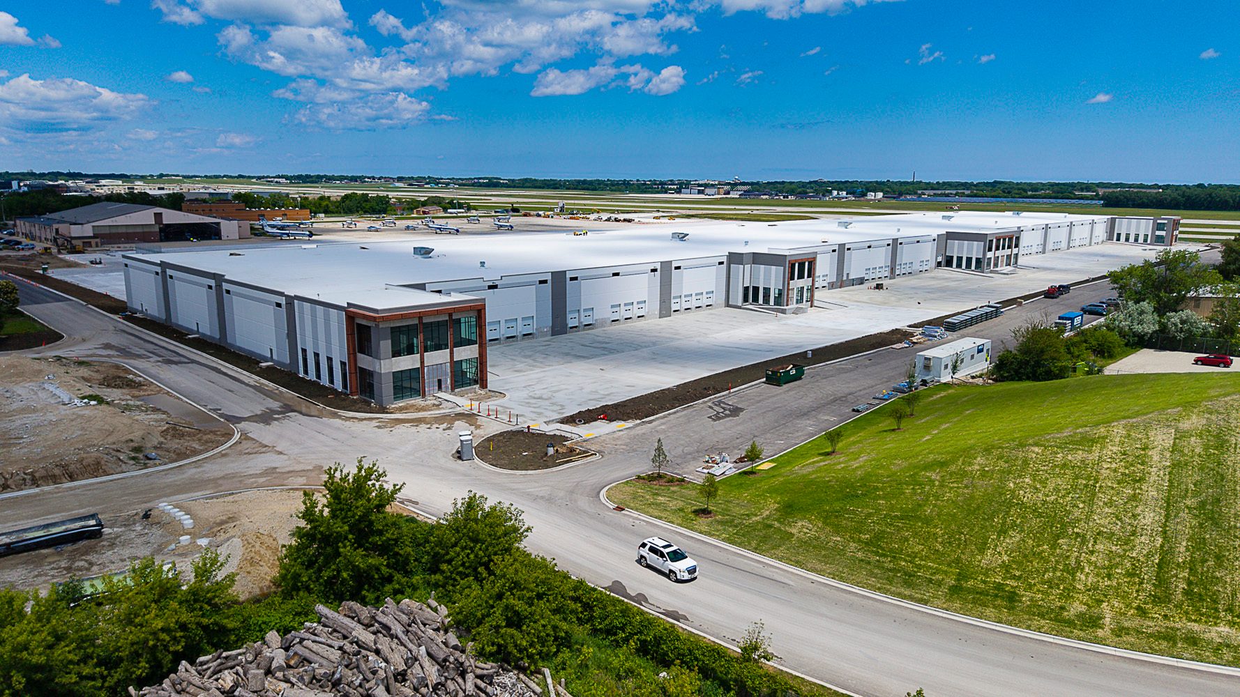 Aerial view of a large modern industrial building complex next to an airport with airplanes on the tarmac.