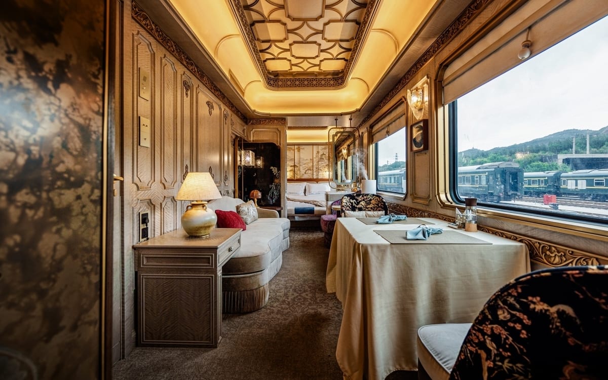 Luxurious train suite with living, dining, and bedroom areas, ornate decor, and scenic window view.