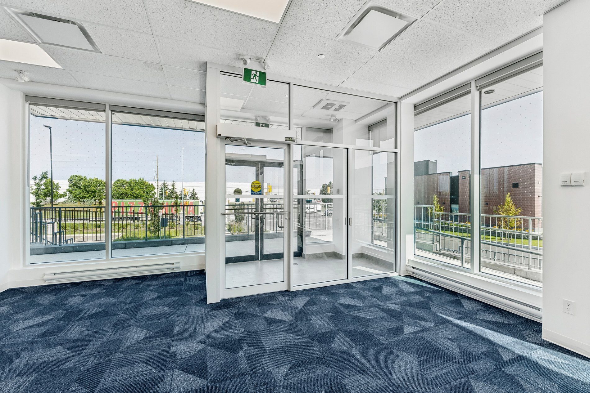 A modern commercial interior with a blue patterned carpet, large windows overlooking greenery, and a central glass entrance.