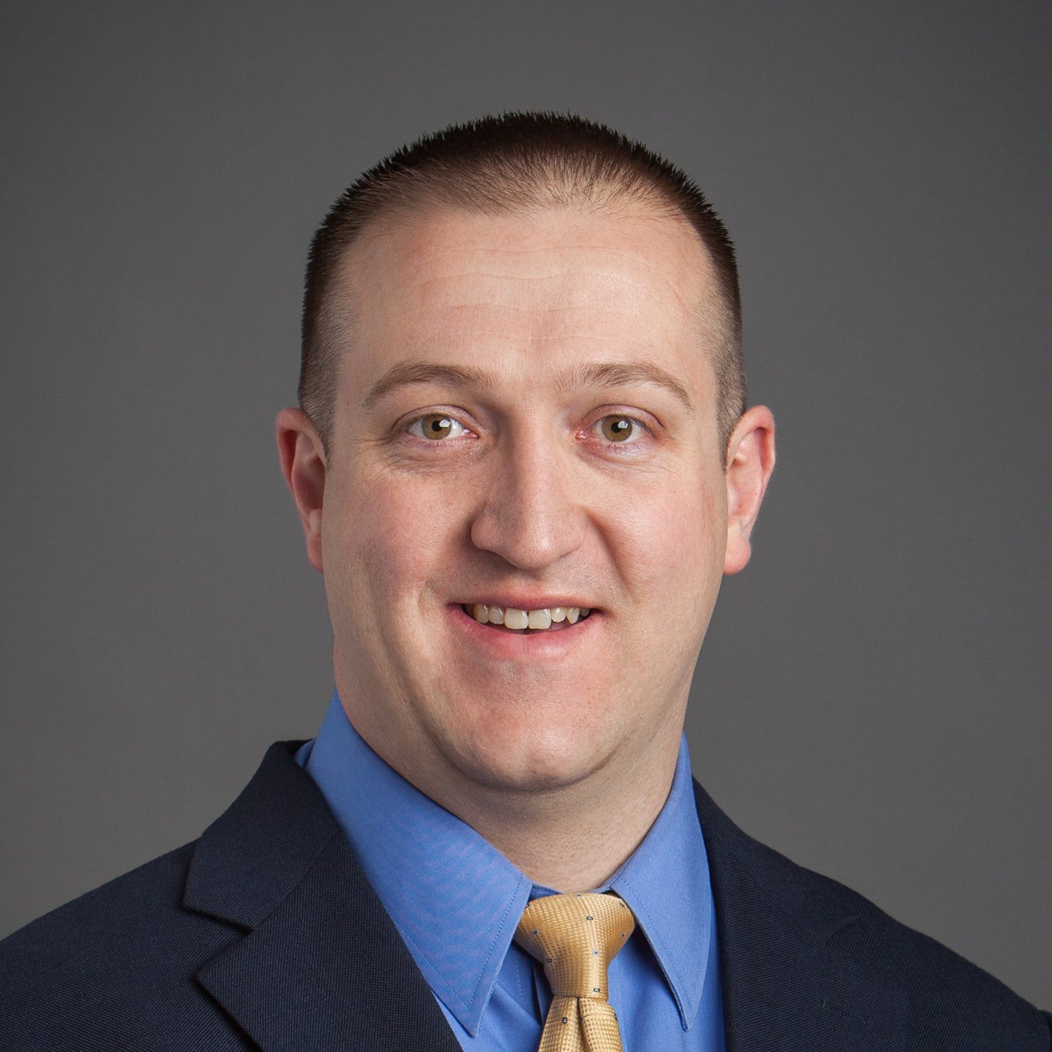 Headshot of a smiling man in a suit, blue shirt, yellow tie.