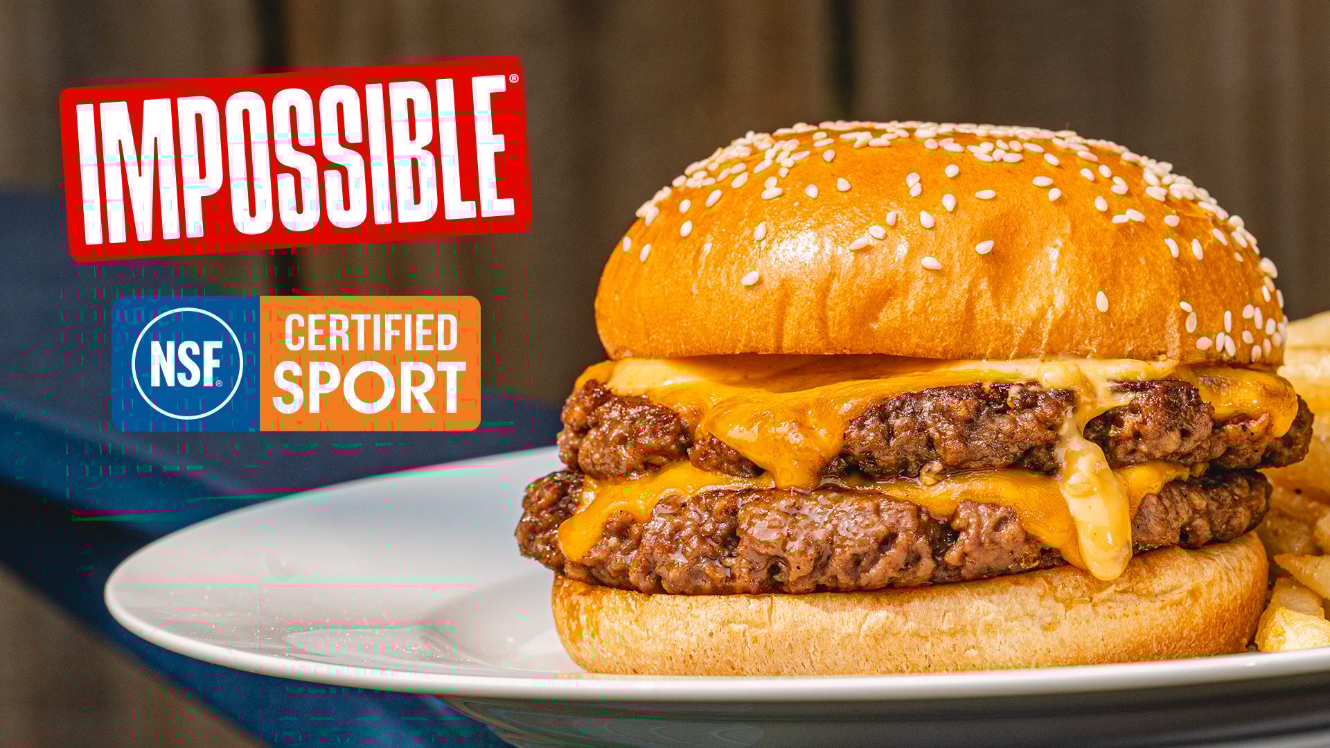 Impossible double cheeseburger with melted cheese, sesame bun, and Impossible and NSF Certified Sport logos.