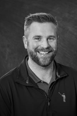 Black and white portrait of a smiling man with a beard and short hair, wearing a casual jacket.