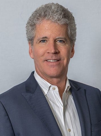Smiling man with curly gray hair, wearing a suit and striped shirt.