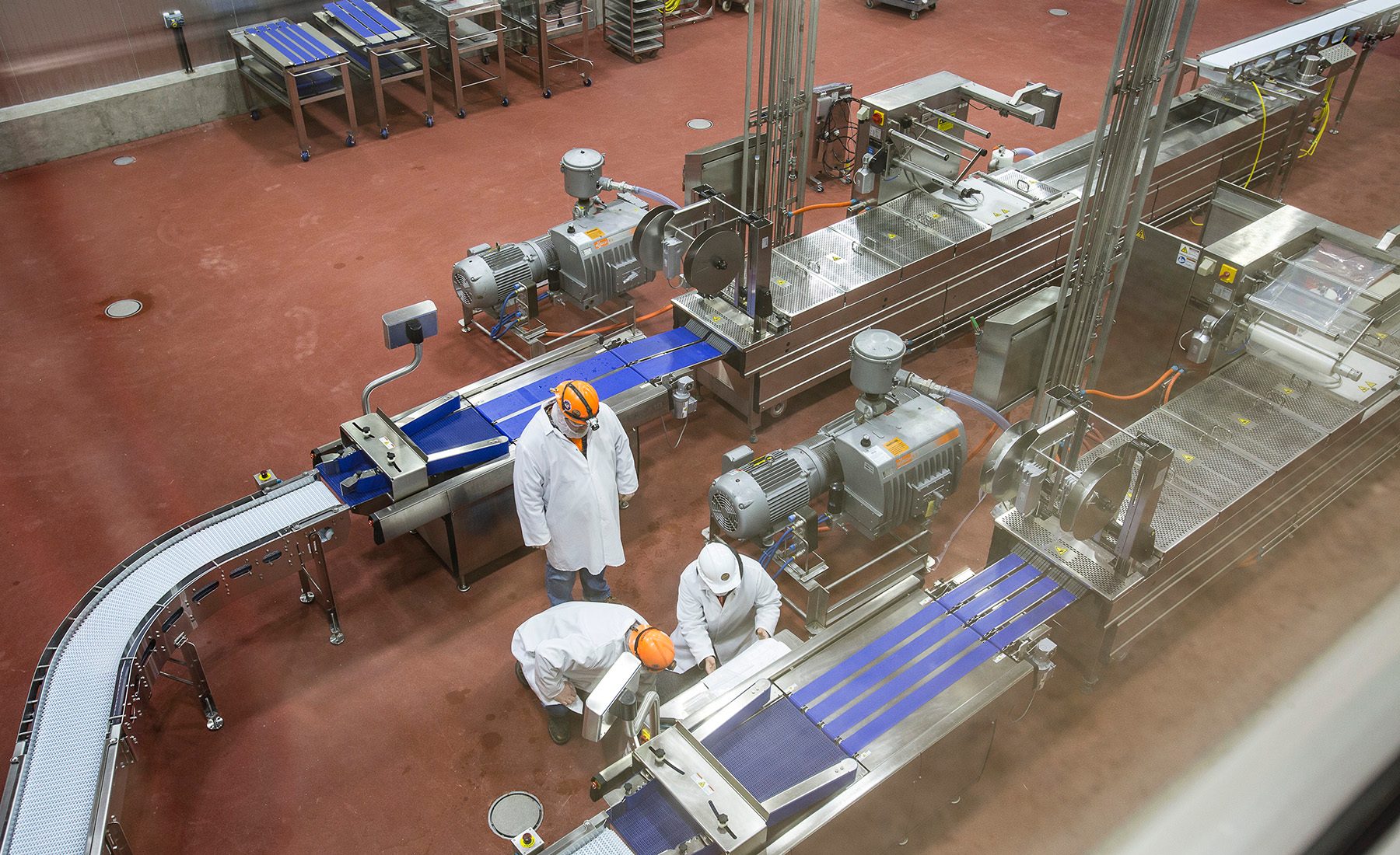Overhead view of a food processing plant with conveyors, machinery, and three workers.