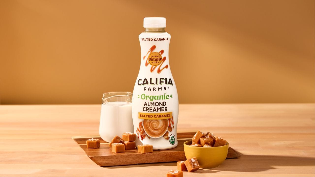Califia Farms Salted Caramel Almond Creamer bottle, milk, and caramel candies on a wooden board.