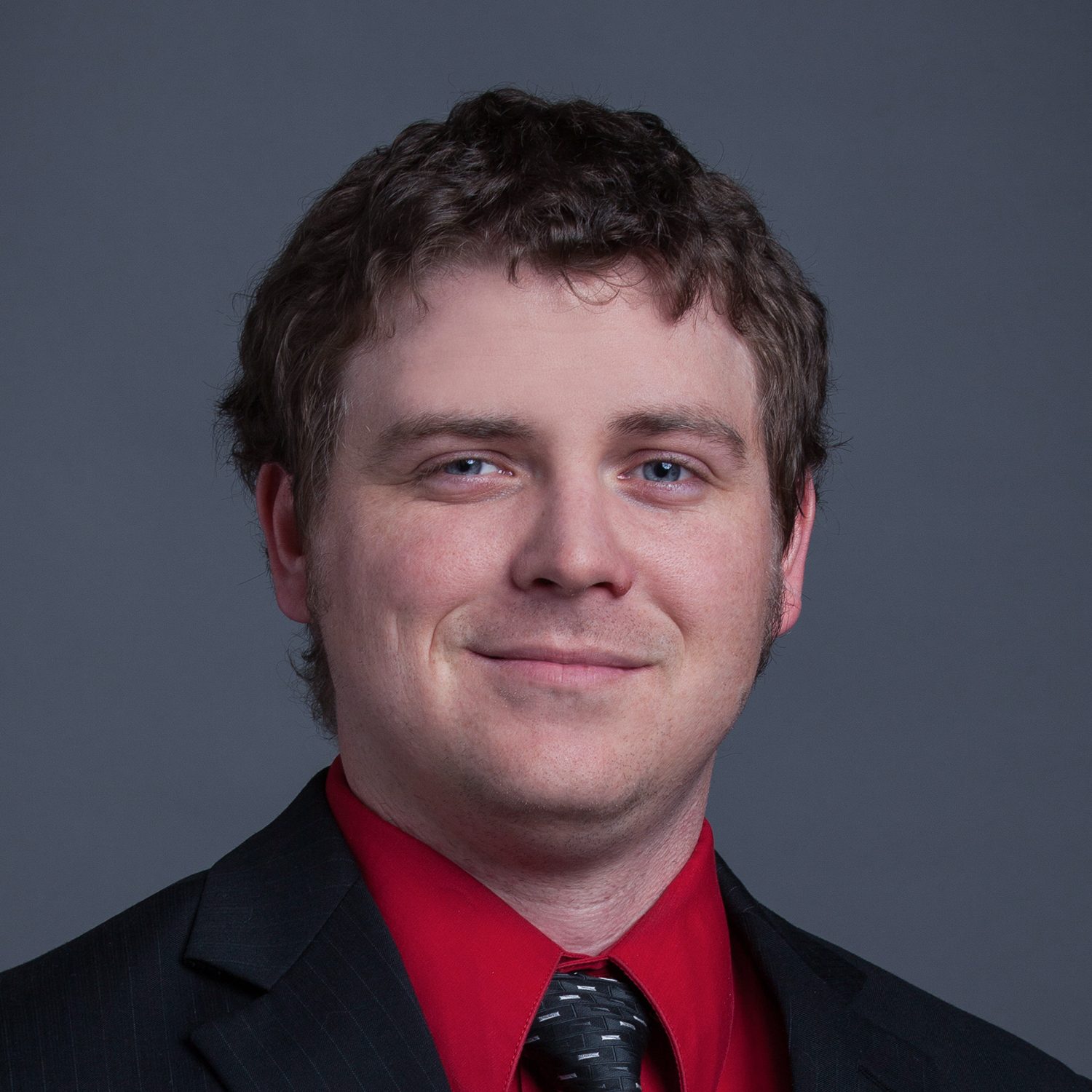 Smiling man in a red shirt and black suit.