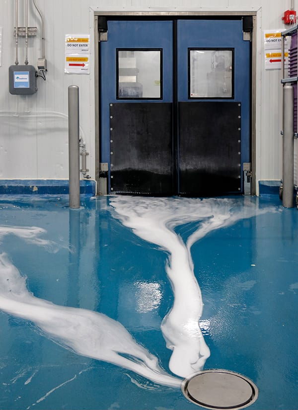 White foam on a blue industrial floor leading to a drain, with blue double doors.