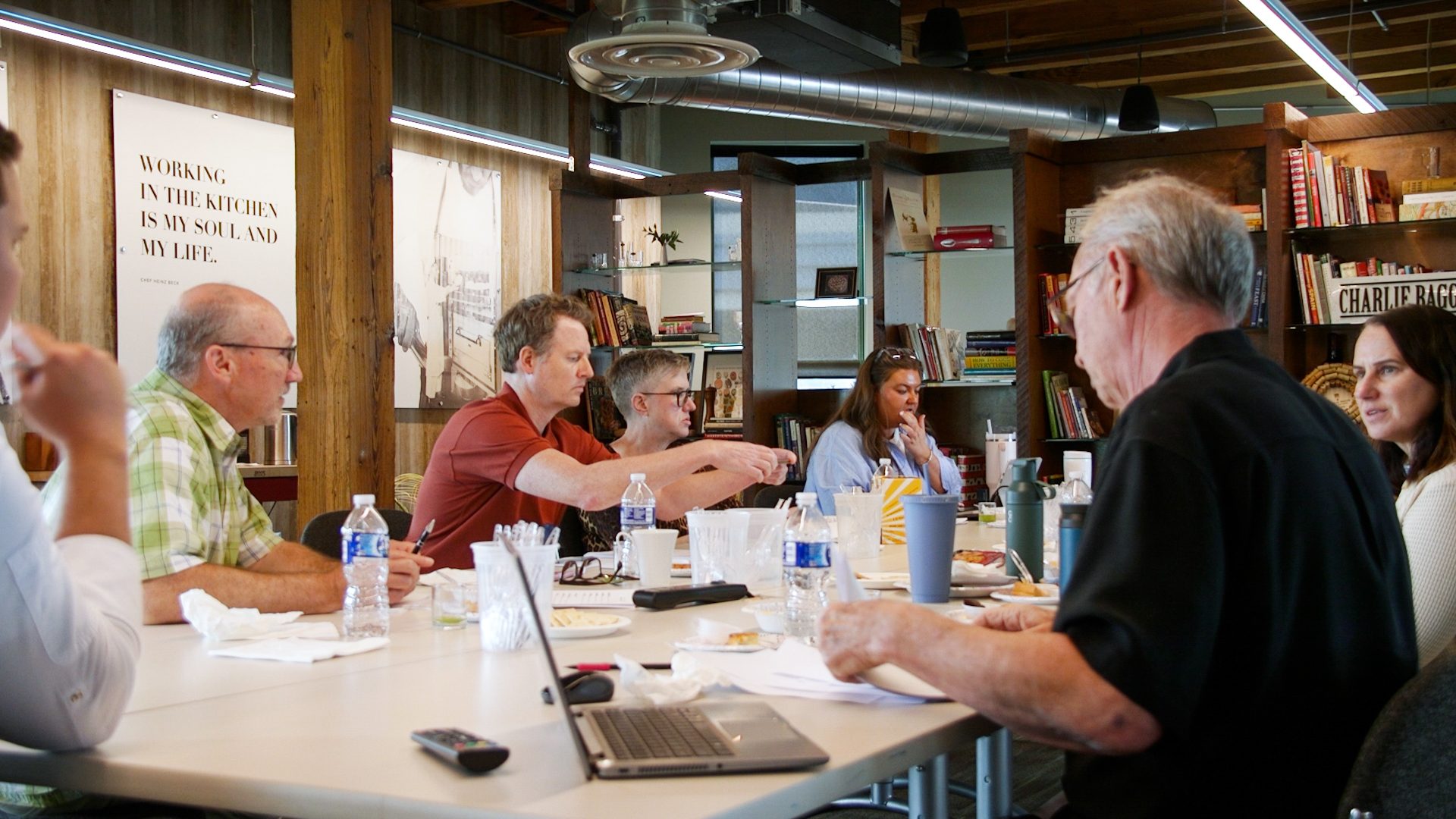 A group of people gathered around a table with snacks and drinks, with a kitchen quote on the wall.