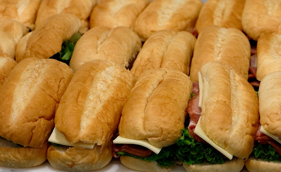 Tray of mini sub sandwiches filled with meat, cheese, and lettuce.