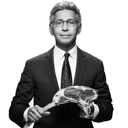 B&W man in suit holding a tomahawk steak.