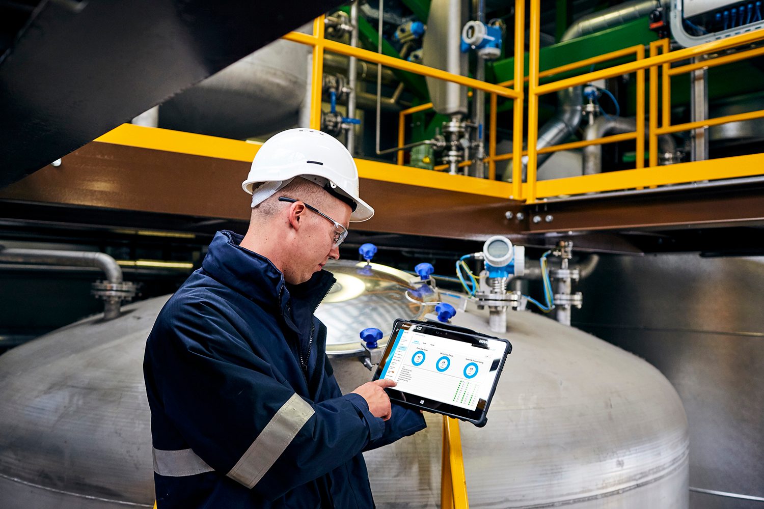 Worker in hard hat uses tablet to monitor industrial equipment.