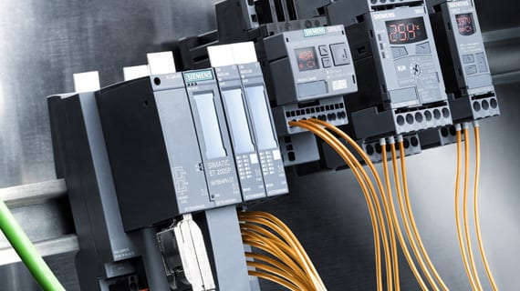 Siemens industrial control modules (SIMATIC ET 200SP and SINAMICS) with orange wiring on a DIN rail.