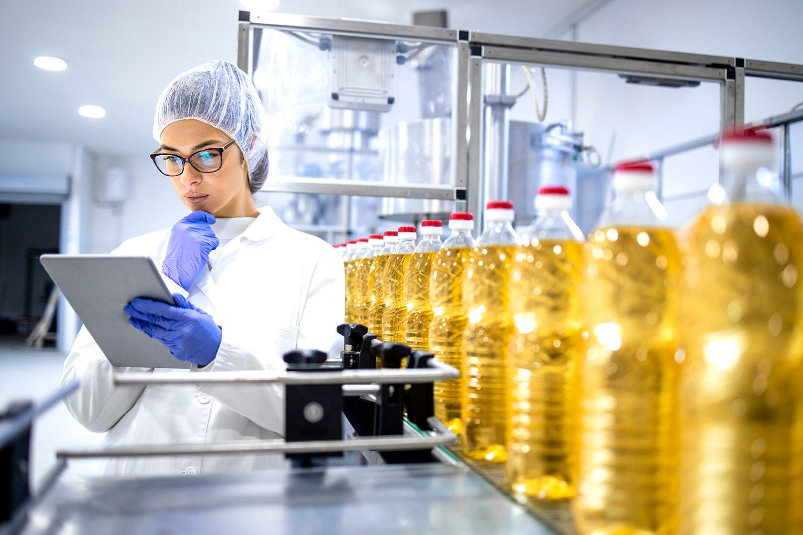 Factory worker with tablet near bottles of oil.