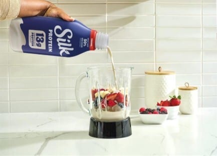 Hand pouring Silk protein milk into a blender with fruit.