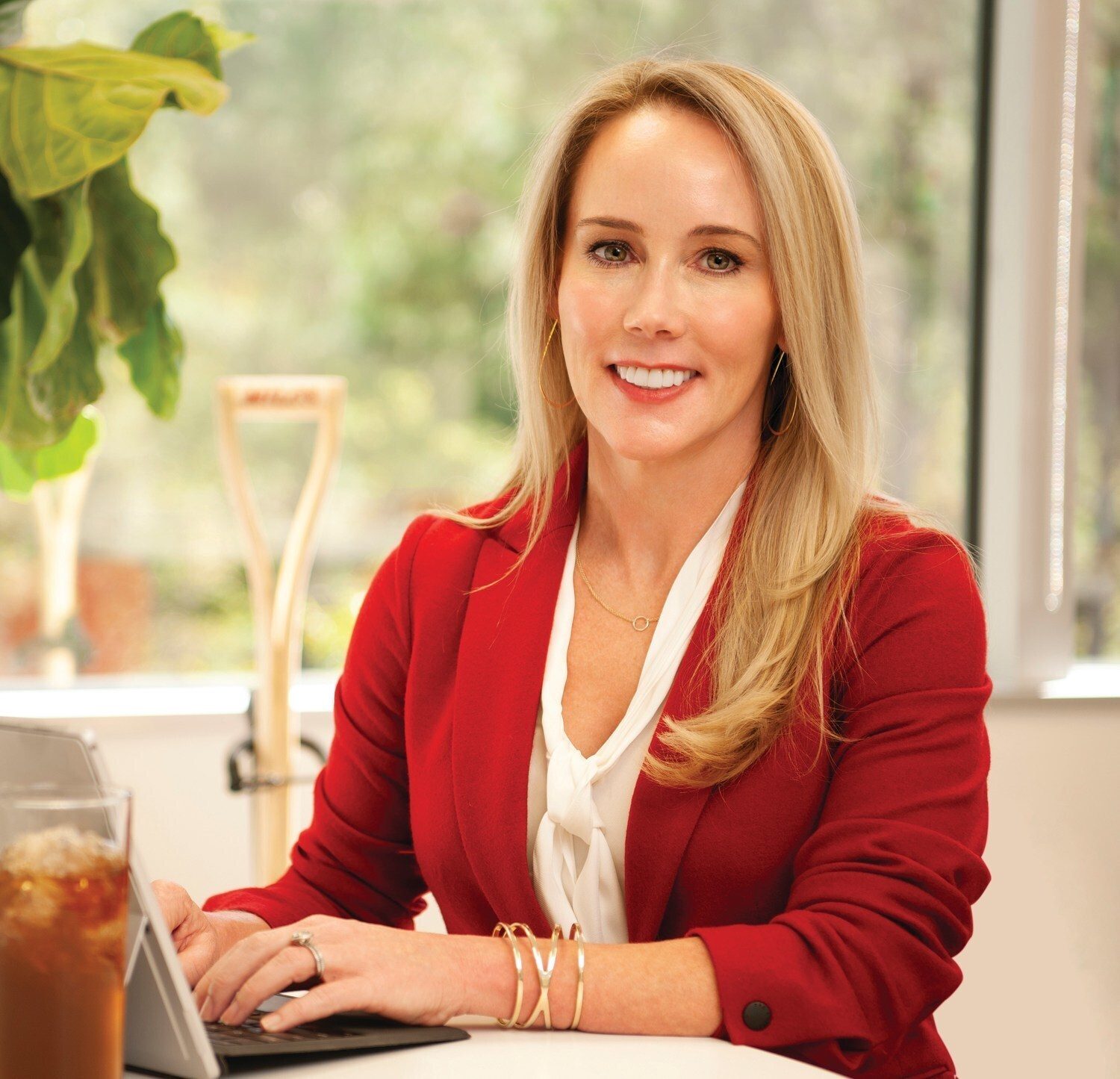 Smiling blonde woman in a red blazer typing on a laptop.