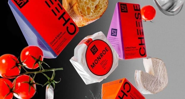 A vibrant still life of various cheese packages, fresh bread, and cherry tomatoes against a split background.