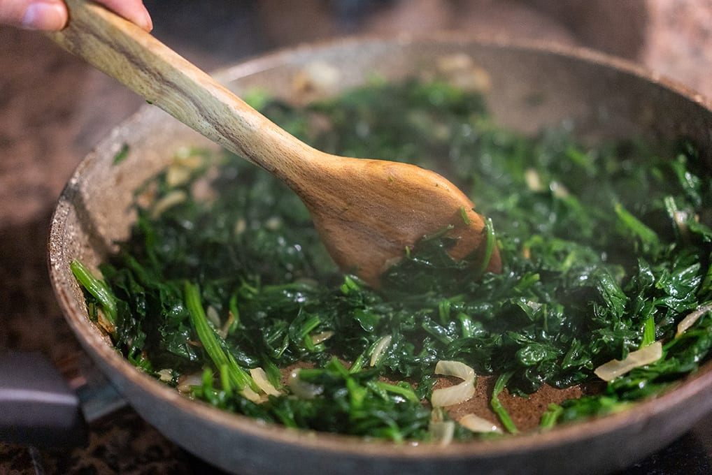 Stirring spinach and onions in a pan.