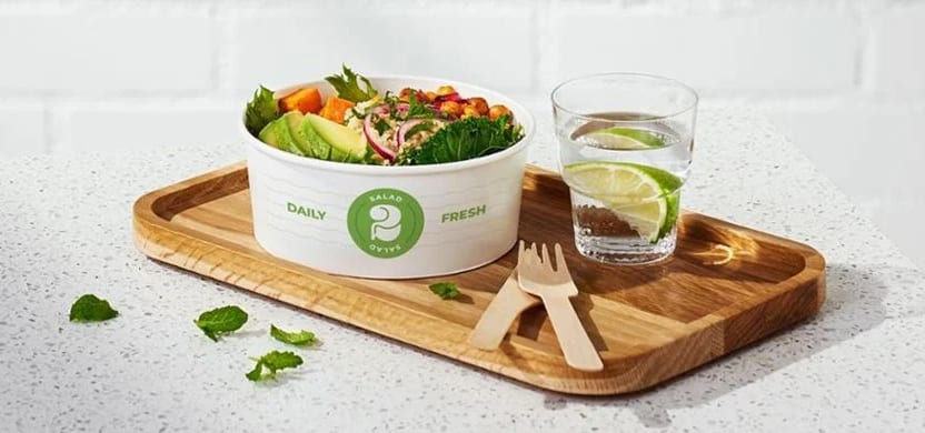 A vibrant salad in a white bowl, glass of lime water, and wooden cutlery on a wood tray.