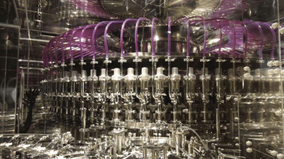 Intricate industrial filling machine with numerous clear nozzles and purple tubing in a sterile environment.