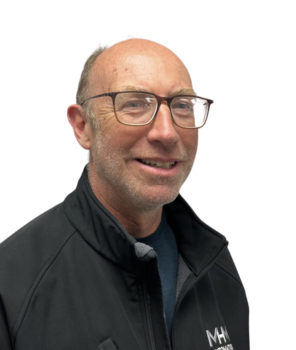 A smiling bald man with glasses and a beard wears a black jacket against a white background.