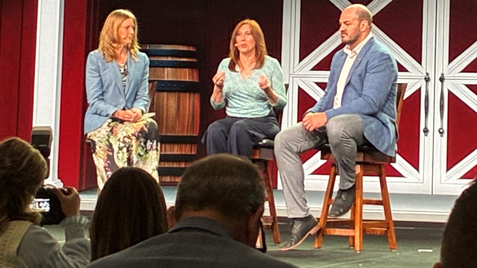 Three speakers on a stage with a red and white barn backdrop.