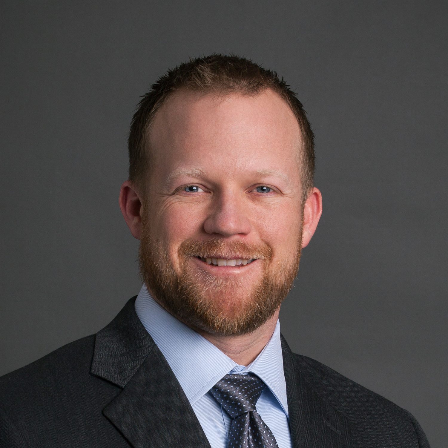 Smiling man headshot: beard, blue eyes, suit & tie.